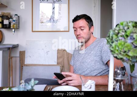 Mann mit Handy, während am Tisch zu Hause sitzen Stockfoto