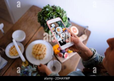 Aus der Perspektive einer Frau, die Waffeln auf dem Teller fotografiert Tisch zu Hause Stockfoto