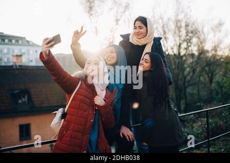 Glückliche junge muslimische Frau, die Selfie mit Freunden durch Geländer In der Stadt Stockfoto