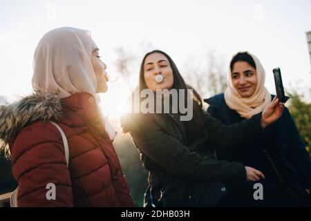 Multiethnische Freundinnen, die beim Selfie gegen Kaugummis blasen Himmel Stockfoto