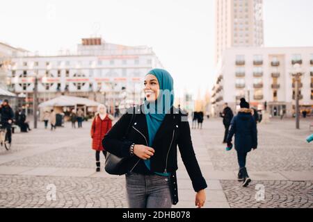 Lächelnde junge muslimische Frau trägt Hijab zu Fuß in Stadt Stockfoto
