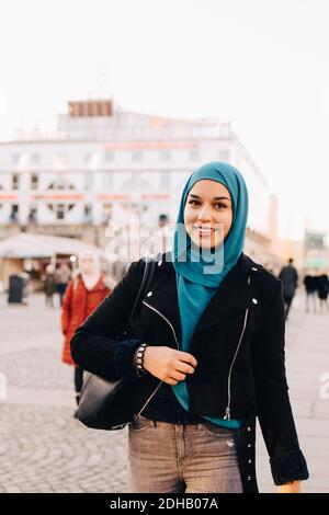 Porträt einer lächelnden jungen muslimischen Frau mit Hijab beim Gehen Fußweg in der Stadt Stockfoto