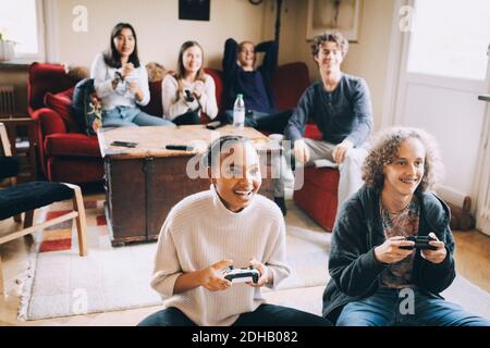 Glückliche Jugendliche spielen Videospiel, während Freunde auf dem Sofa sitzen Im Wohnzimmer Stockfoto