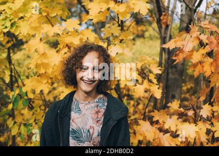 Fröhlicher Teenager mit Zahnspangen und lockigen Haaren, die wegschauen Im Herbst Stockfoto