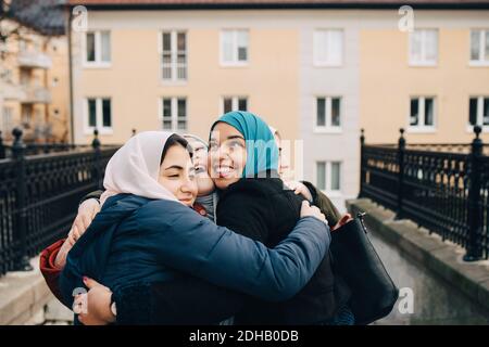 Fröhliche multiethnische weibliche muslimische Freunde umarmen in der Stadt Stockfoto