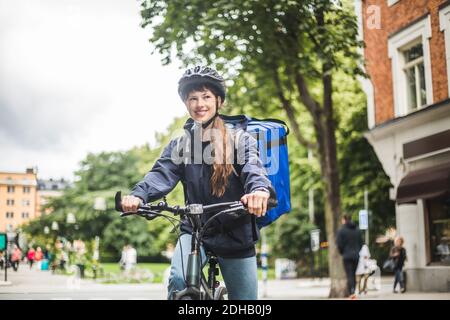 Lächelndes Essen Lieferung Frau mit Fahrrad auf der Straße in der Stadt Stockfoto