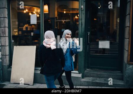 Glückliche junge Frau winkt beim Gehen mit Freund auf Bürgersteig In der Stadt Stockfoto