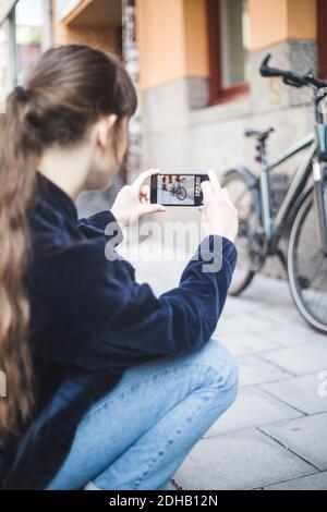 Junge Frau fotografiert Fahrrad auf Fußweg Stockfoto