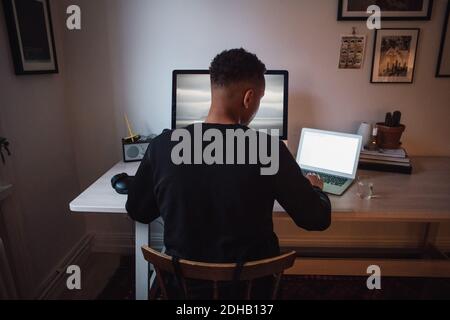 Rückansicht des jungen freiberuflichen Arbeiters mit Laptop und Computer Am Schreibtisch Stockfoto
