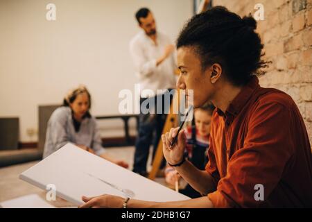 Nachdenkliche junge Künstler Malerei auf Leinwand mit Freunden im Hintergrund Stockfoto