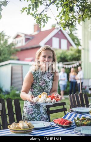 Porträt von lächelnden reifen Frau hält Teller an Tisch Im Hinterhof Stockfoto