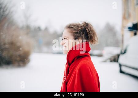 Seitenansicht einer lächelnden jungen Frau im roten Pullover im Stehen Auf schneebedecktem Feld Stockfoto