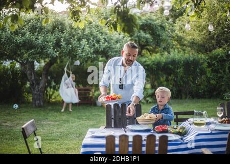 Reifer Vater Regie Sohn mit Teller beim Zeigen auf Tisch im Hof Stockfoto