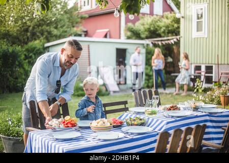 Vater im Gespräch mit Sohn, während der Anordnung Teller auf dem Tisch Im Hinterhof Stockfoto