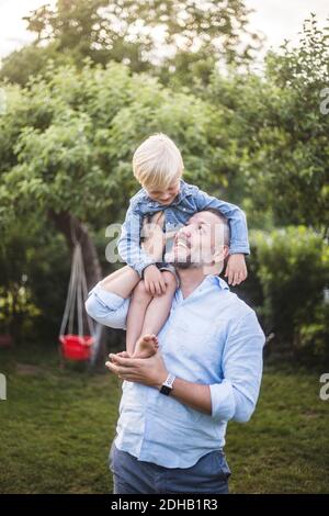 Glücklicher Vater trägt Sohn auf Schultern im Hinterhof Stockfoto