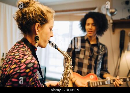 Männliche und weibliche Freunde spielen Saxophon und Gitarre beim Üben Im Aufnahmestudio Stockfoto