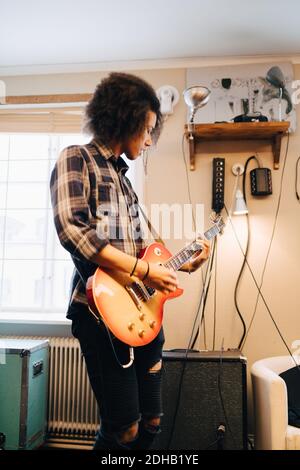 Junger Mann spielt Gitarre, während er im Aufnahmestudio praktiziert Stockfoto