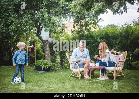 Eltern schauen Jungen spielen mit Fußball im Hinterhof Stockfoto