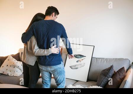 Rückansicht des jungen Paares umarmt, während die Wahl Malerei auf Sofa zu Hause Stockfoto