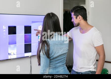 Junges Paar mit Touchscreen-Fernseher an der Wand montiert in Wohnzimmer Stockfoto