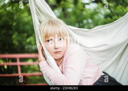 Nachdenkliches Mädchen, das wegschaut, während es auf weißem Schaukel sitzt Garten Stockfoto