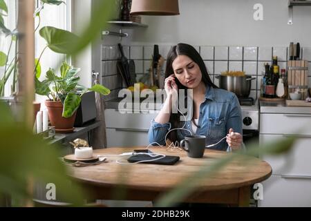 Junge Frau hört Musik über Kopfhörer, während sie am Tisch sitzt Stockfoto