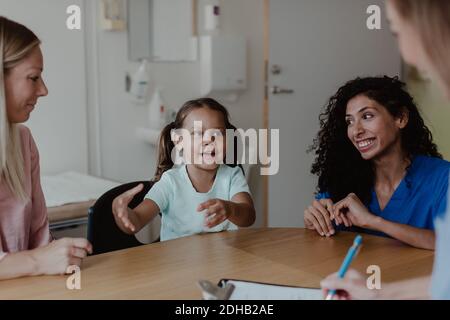 Mädchen im Gespräch mit Arzt, während lächelnd Mutter und Krankenschwester suchen Bei ihr im Krankenhaus Stockfoto