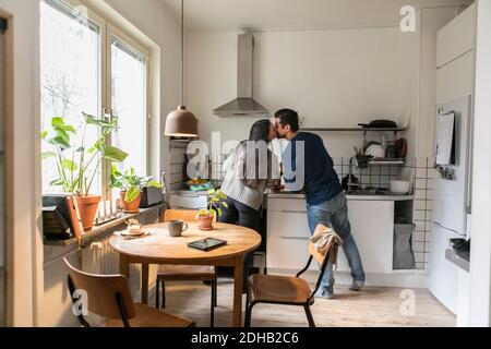 Lächelndes Paar küsst während der Arbeit in der Küche zu Hause Stockfoto