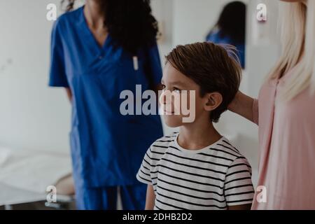 Lächelnder Junge steht bei der Mutter, während Krankenschwester im Hintergrund Im Krankenhaus Stockfoto