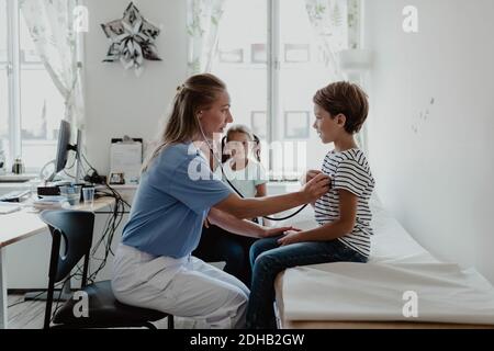 Ärztin hört dem Herzschlag des Jungen zu, während die Familie darin sitzt Medizinischer Raum Stockfoto