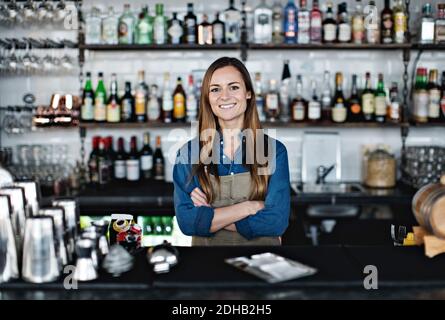 Porträt einer lächelnden Besitzerin, die mit gekreuzten Armen steht Check-out-Schalter Stockfoto