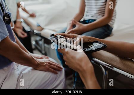 Beschnittene Hände der Krankenschwester, die Glaukome vom Arzt hält, während Junge Sitzen im Untersuchungsraum Stockfoto