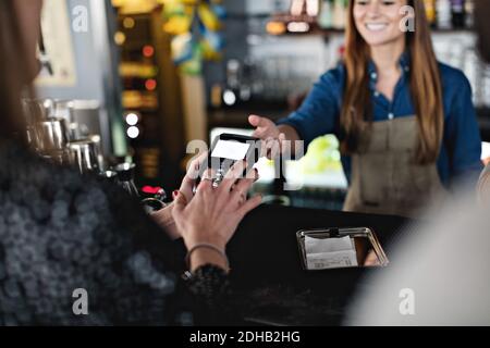 Weibliche Kundin, die kontaktlos mit der lächelnden Besitzerin an der Kasse bezahlt Zähler Stockfoto