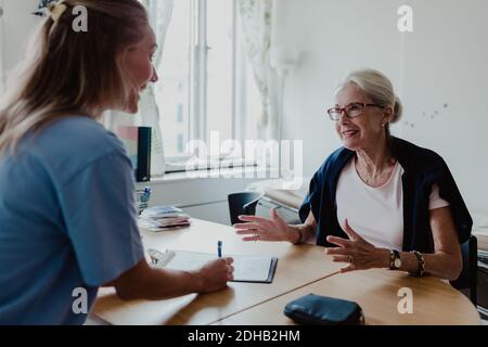 Lächelnder Arzt schreibt Rezept, während ältere Frau in hören Krankenhaus Stockfoto