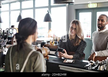 Frau, die im Stehen Kreditkartenzahlung an weibliche Besitzerin macht Von einem Mann an der Kasse Stockfoto