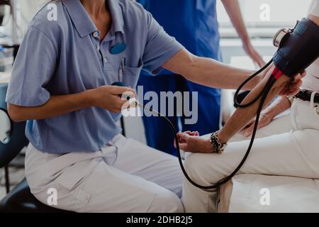 Mittelteil der Ärztin, die den Blutdruck des älteren Patienten überprüft Im medizinischen Raum Stockfoto