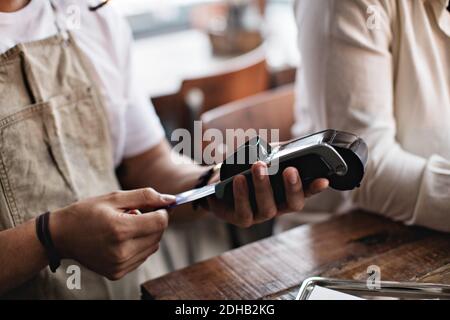 Besitzer mit Kreditkarte Leser, während stehen bei männlichen Kunden Am Tisch Stockfoto