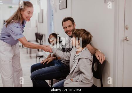 Lächelnd Frau Kinderarzt Handshake mit Junge sitzt mit Familie in Krankenhausflur Stockfoto