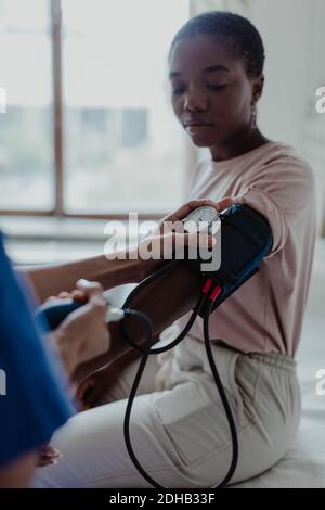 Beschnittene Hände einer Krankenschwester, die den Blutdruck von jungen Menschen überprüft Patient im medizinischen Raum Stockfoto