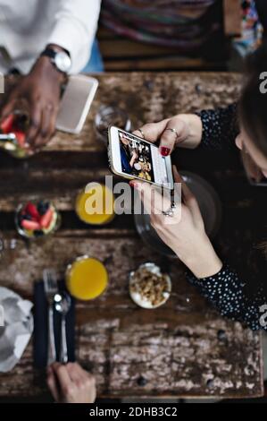 Weitwinkelansicht einer Frau, die mit dem Smartphone Lebensmittel fotografiert Am Tisch Stockfoto