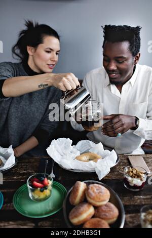 Junge Frau gießt Milch in Glas von Mann sitzen gegen Wand am Restaurant Stockfoto