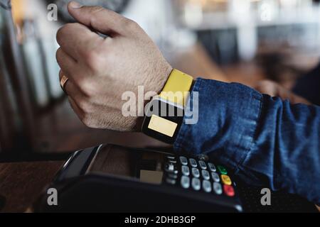 Zugeschnittenes Bild des Kunden, der kontaktlos über Smart Watch bezahlt Am Barschalter Stockfoto