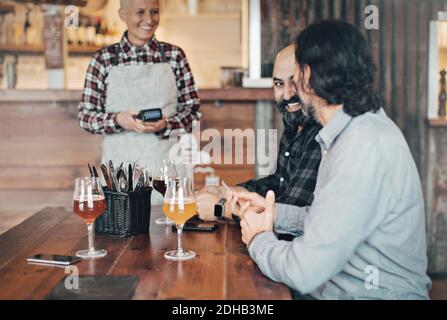 Barkeeper mit Kreditkartenleser im Gespräch mit männlichen Kunden Am Tisch in der Bar Stockfoto