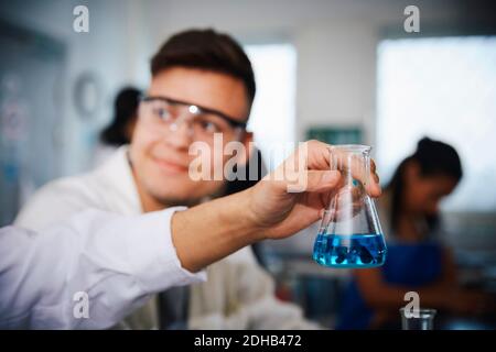 Beschnittene Hand des männlichen Studenten, der Lösung in konischen Kolben hält Von einem Freund im Chemielabor Stockfoto