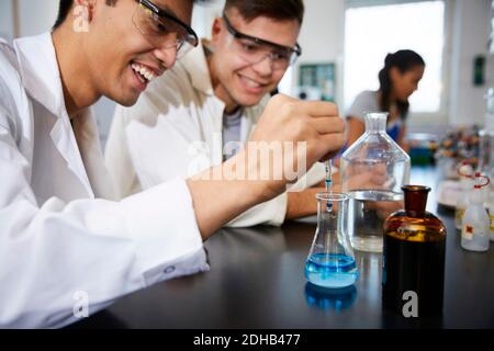 Lächelnde junge männliche Studenten mischen Lösungen in Glaswaren bei Chemie Labor Stockfoto