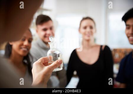 Zugeschnittenes Bild von reifen Lehrerin, die Lösung in Glaswaren hält Beim Erklären junger multiethnischer Studenten in Stockfoto
