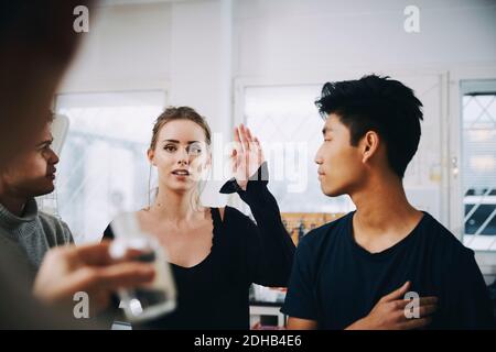 Junge Studentin, die mit erhobener Hand inmitten von Männchen steht, die schauen Bei Lehrer im Chemielabor Stockfoto
