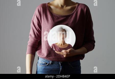 Wer bin ich? Junge Frau, die einen runden Spiegel vor ihrem Körper hält. Der Spiegel zeigt ihr verschwommenes Gesicht. Stockfoto
