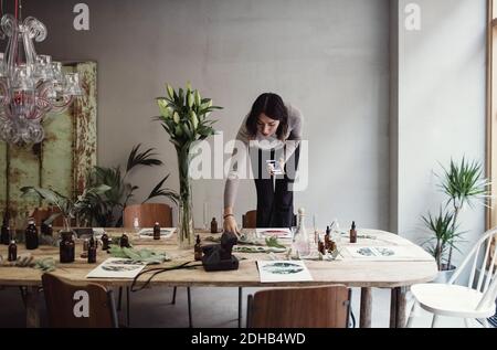Junge Frau, die auf einem Stuhl steht und einen Tisch in der Parfümwerkstatt arrangiert Stockfoto