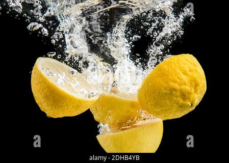 Frische gelbe Zitronen im Wasser spritzen auf schwarzem Hintergrund Stockfoto